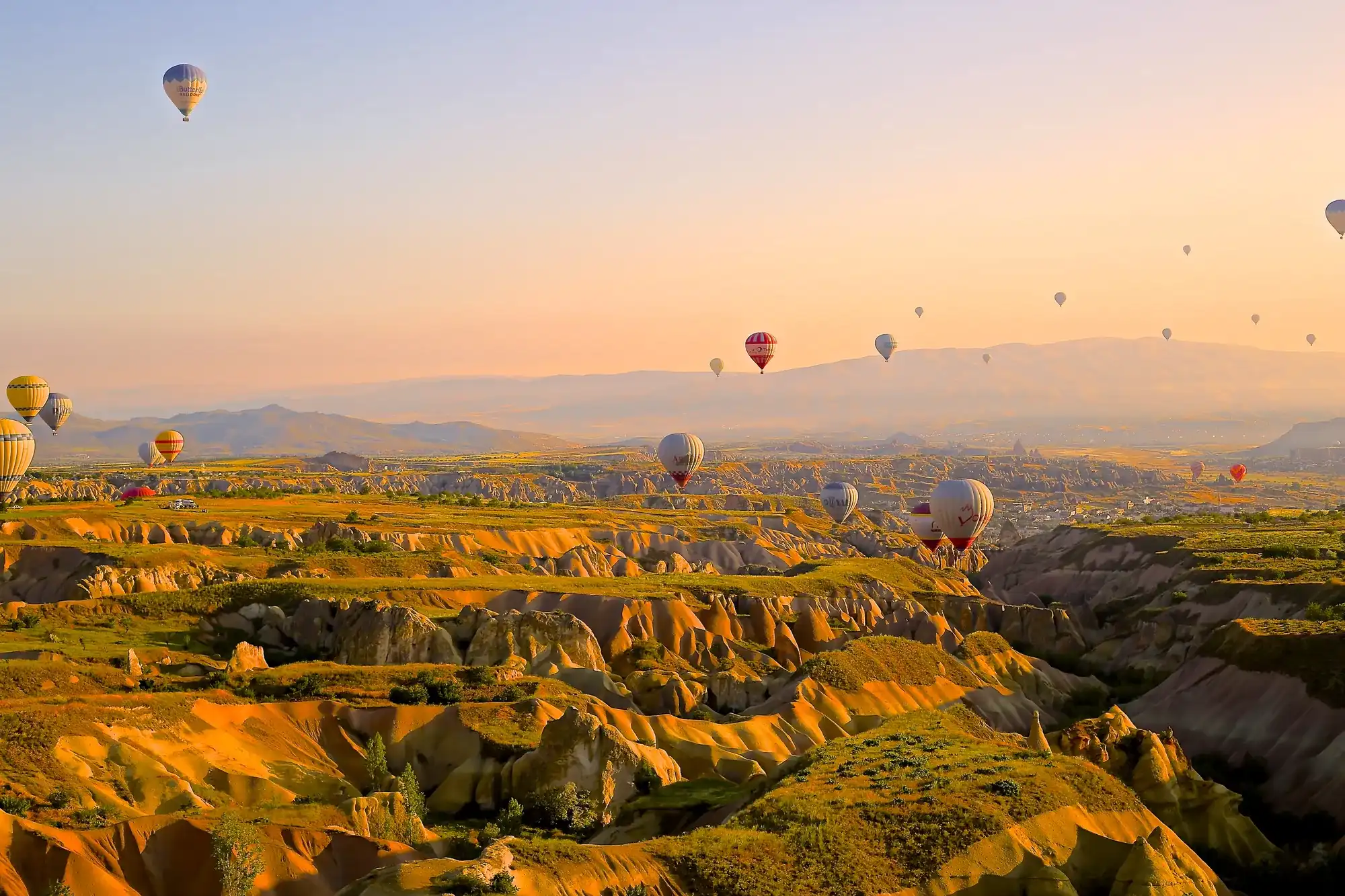 Hot air balloons drifting over Cappadocia's eroded valleys in golden sunrise light.