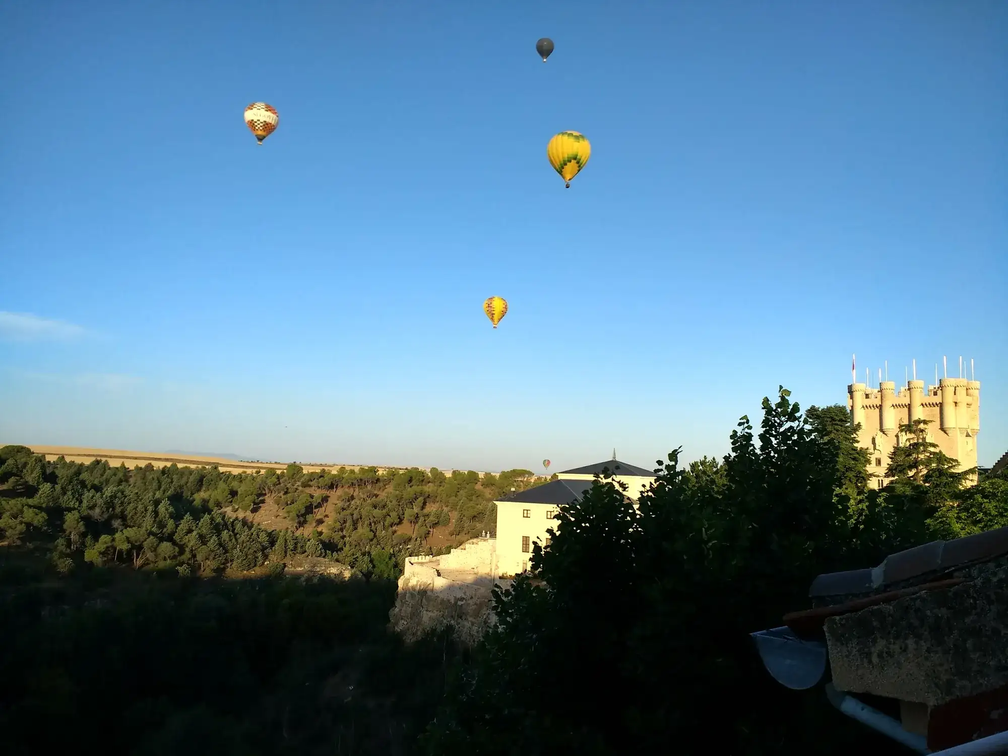 Hot air balloons in a clear sky beside the Alcázar of Segovia, Spain.